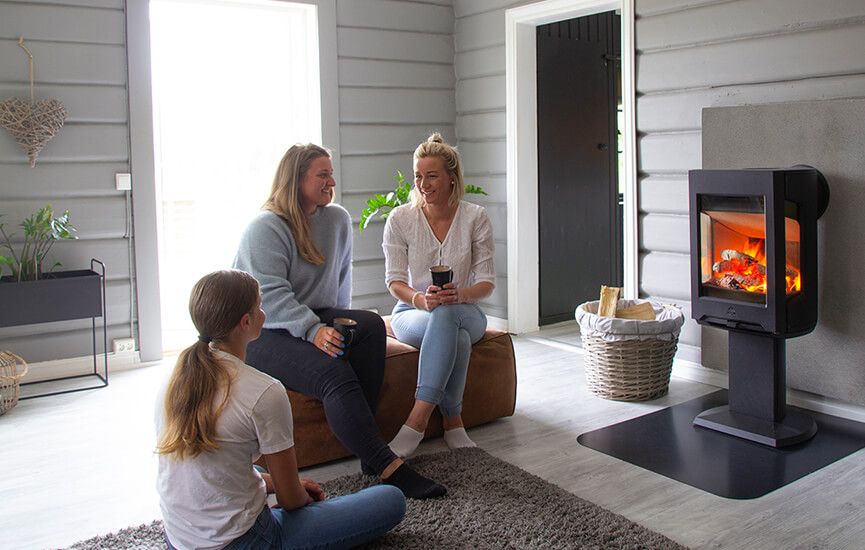Tre personer i stue med moderne vedovn og flammer