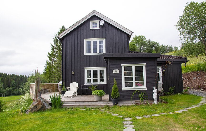 Enebolig med mørk trekledning, terrasse og hage i landlige omgivelser