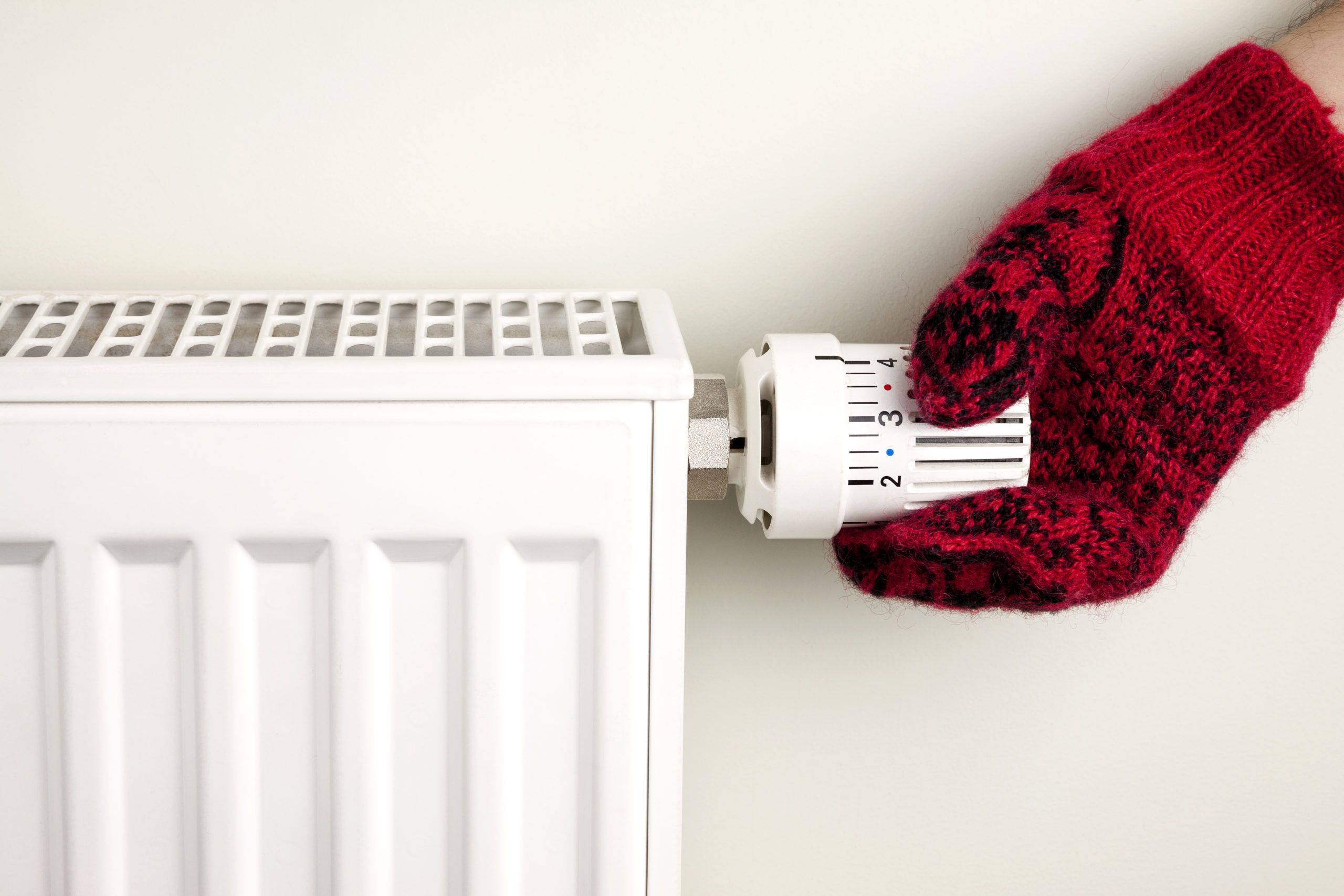 Hånd med strikket vott som justerer termostat på elektrisk radiator