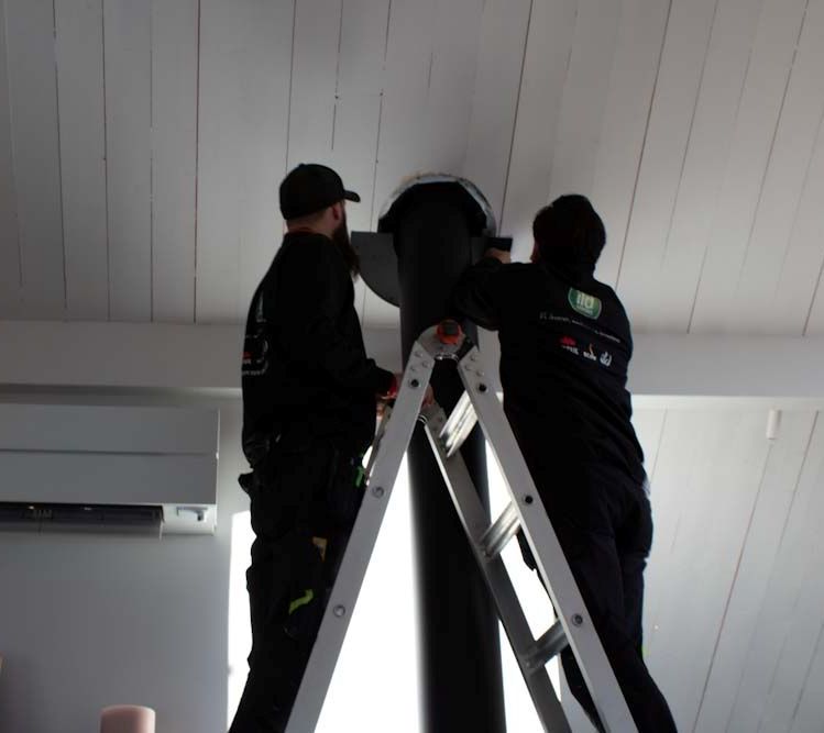 Montering av stålpipe gjennom tak av montører ved installasjon av vedovn