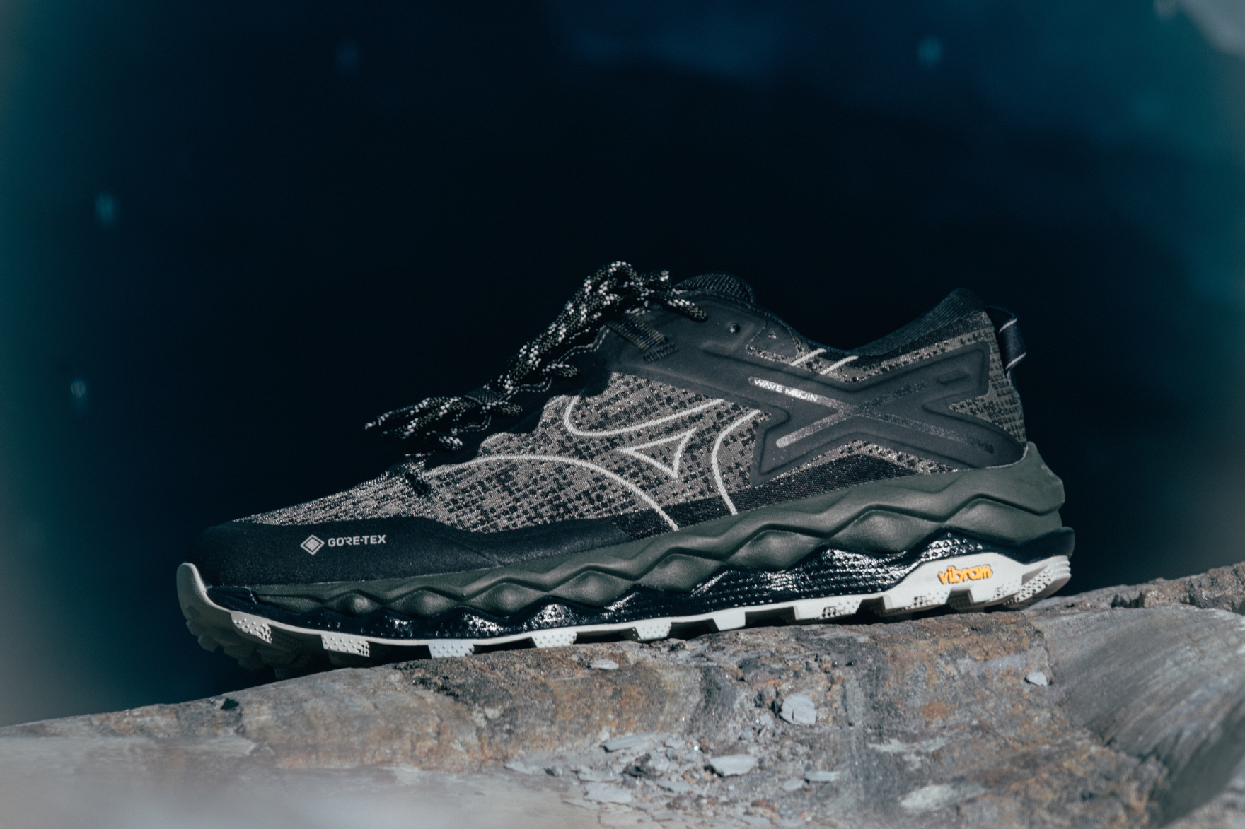 black mizuno sneaker styled on top of rock with black background