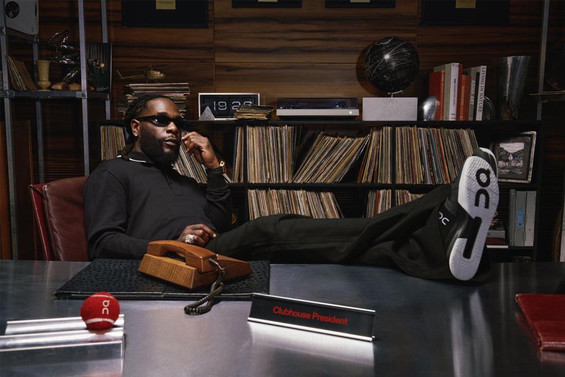 Burna Boy sitting on desk with records in the background
