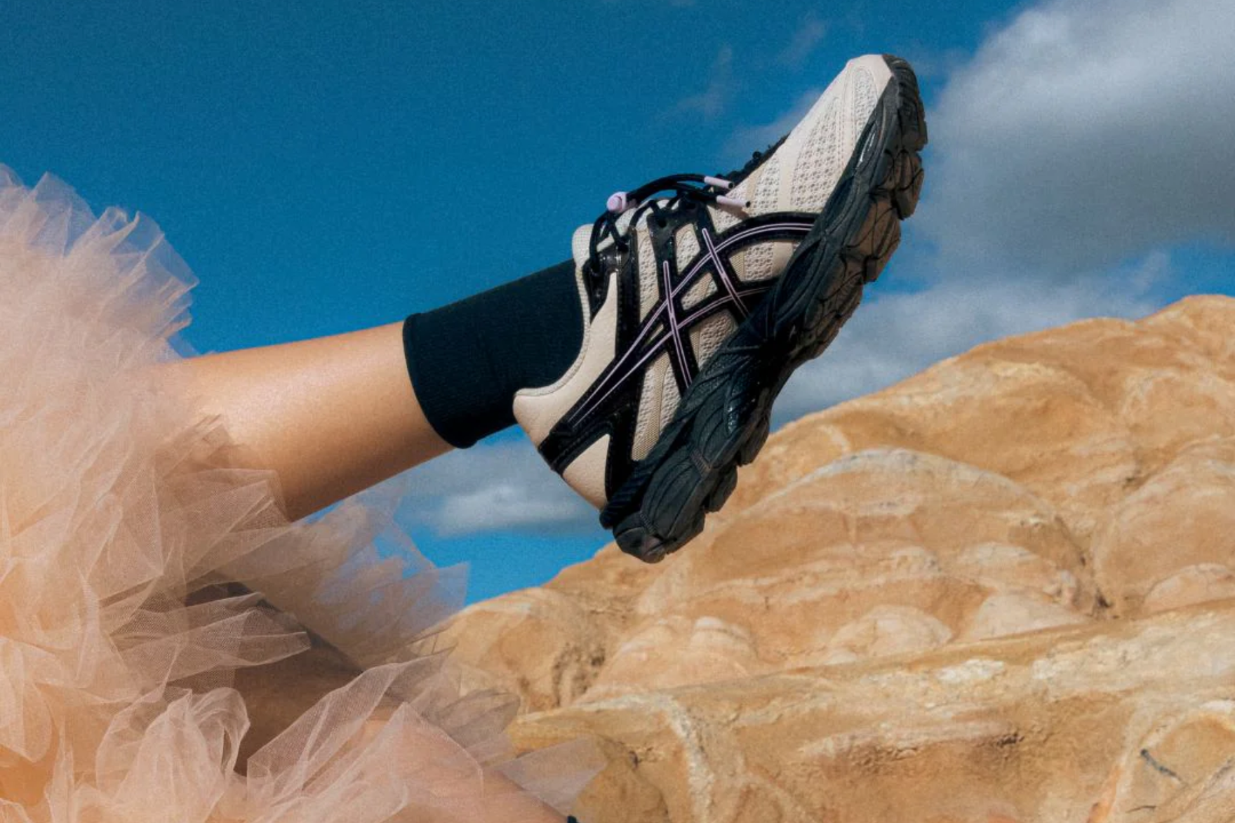 a white asics sneaker held up against desert background