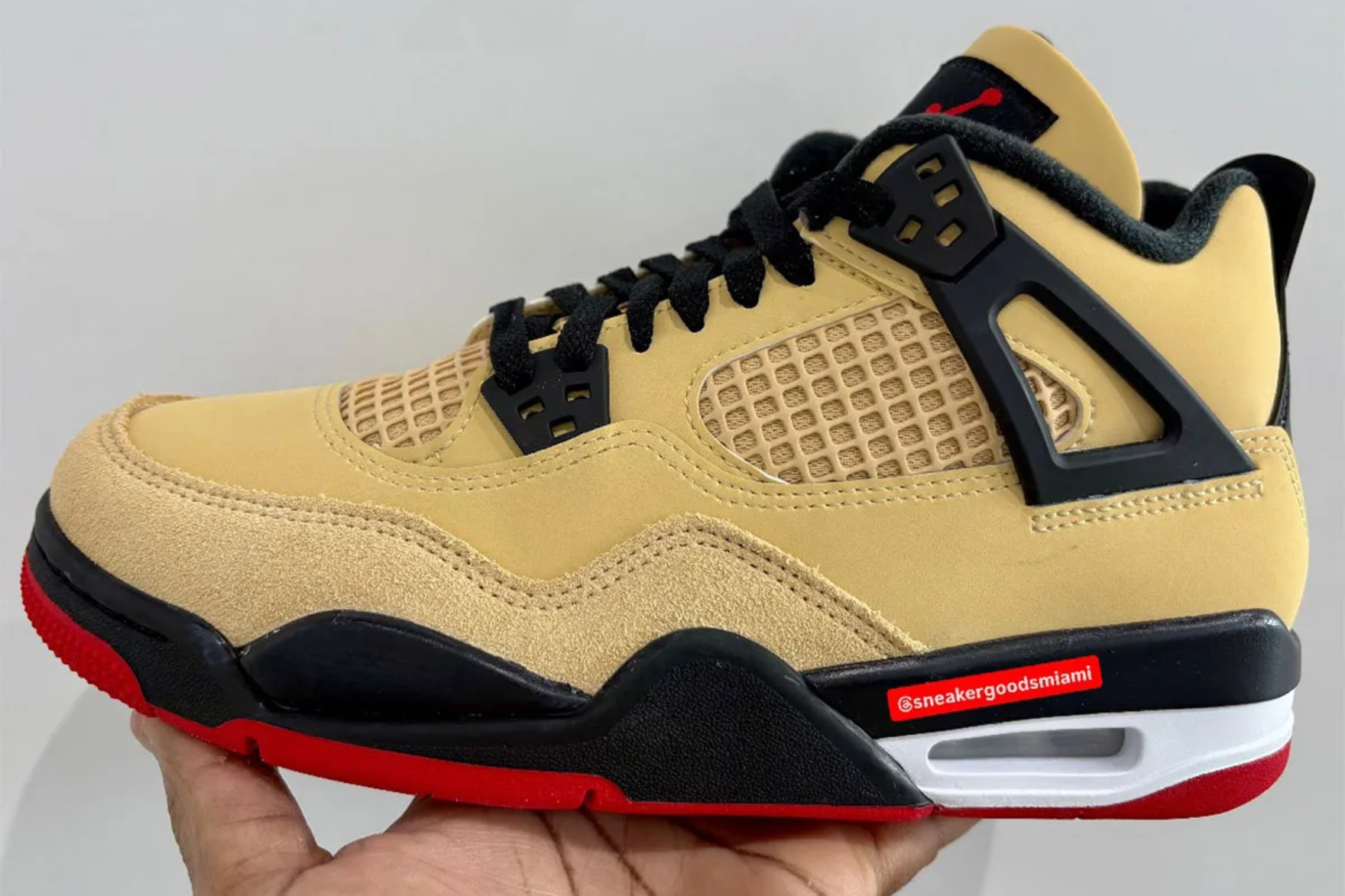 a biege jordan 4 sneaker with black and red sole
