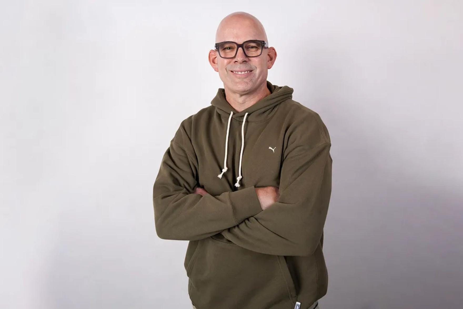 Smiling, bald man with glasses wearing a green PUMA hoodie