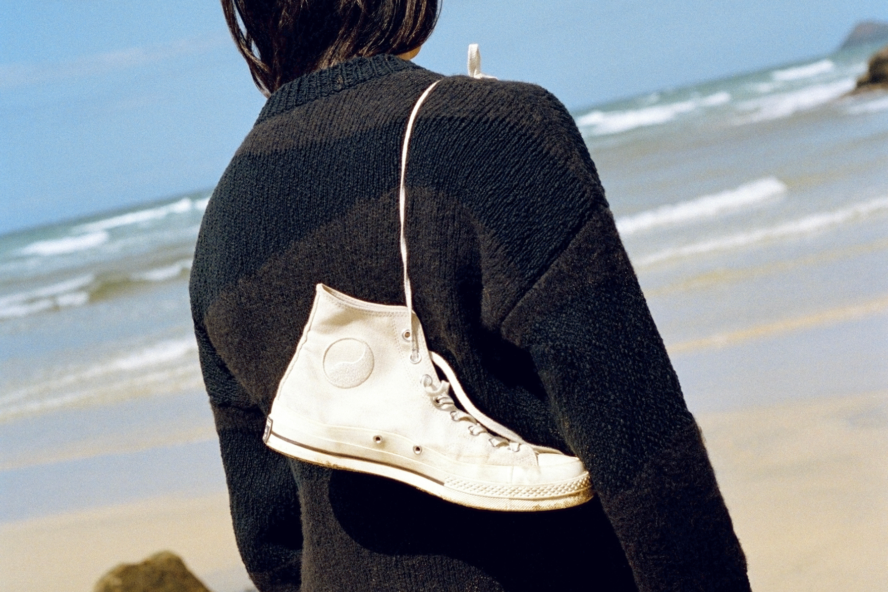 a pair of converse flung over someones shoulder beach shot