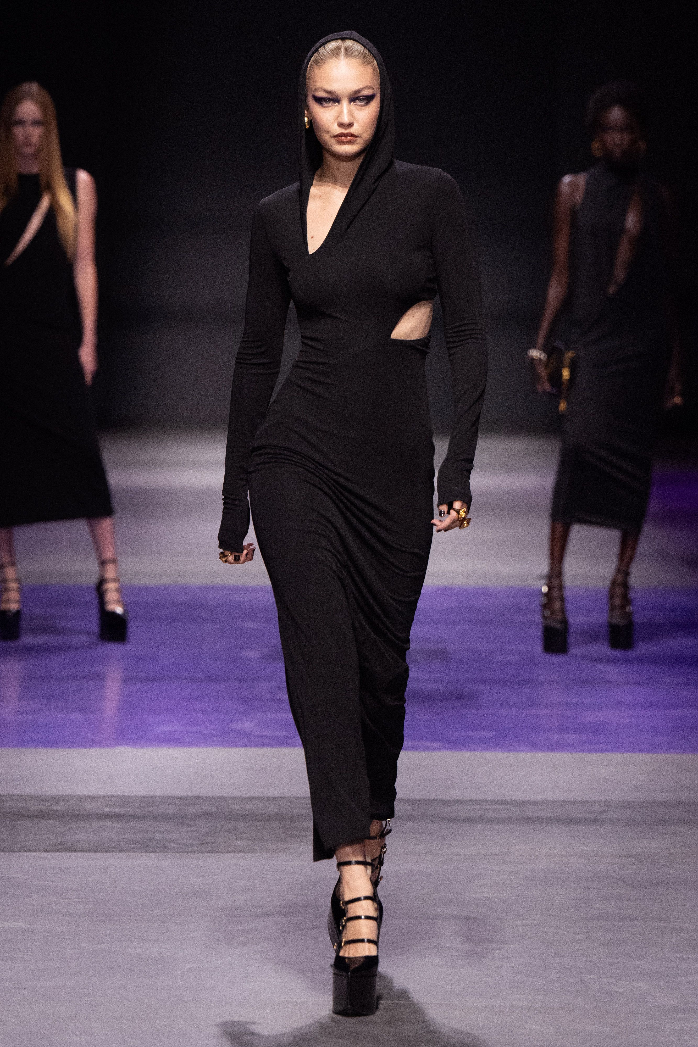 Gigi Hadid walking for Versace wearing a long black hooded dress