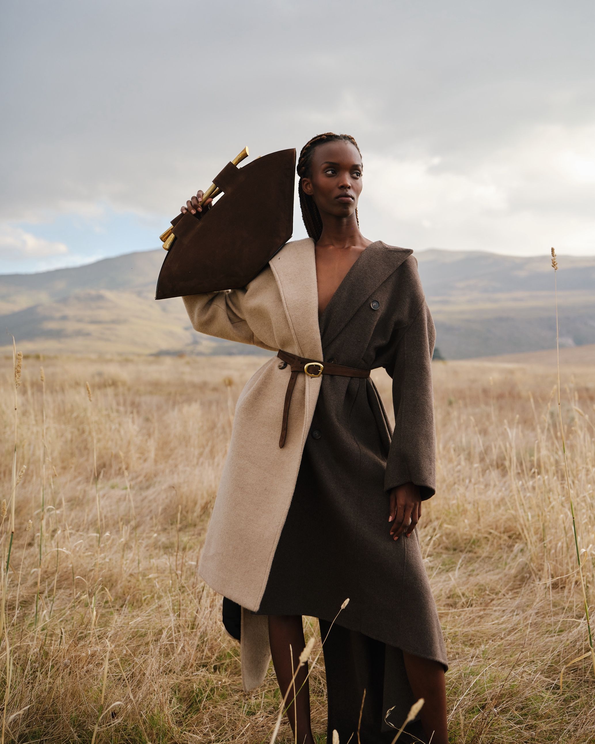 Woman holding bag, in field, wearing statement coat. 