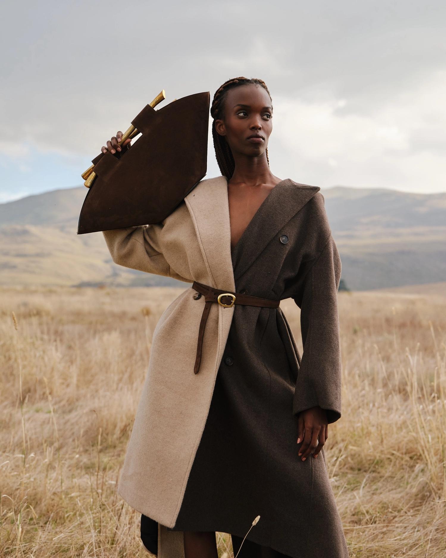 Woman holding bag, in field, wearing statement coat.