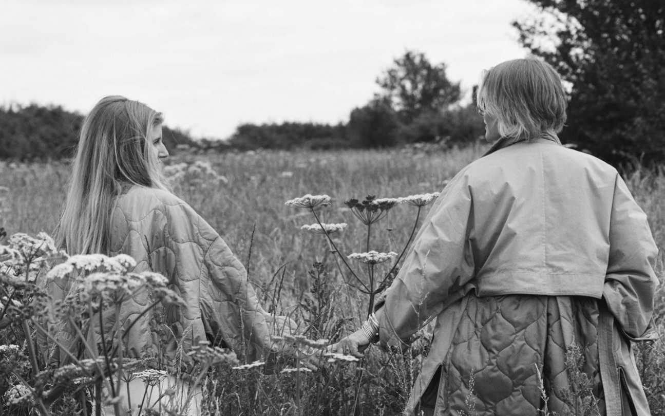 Two people in padded jackets holding hands in flower meadow