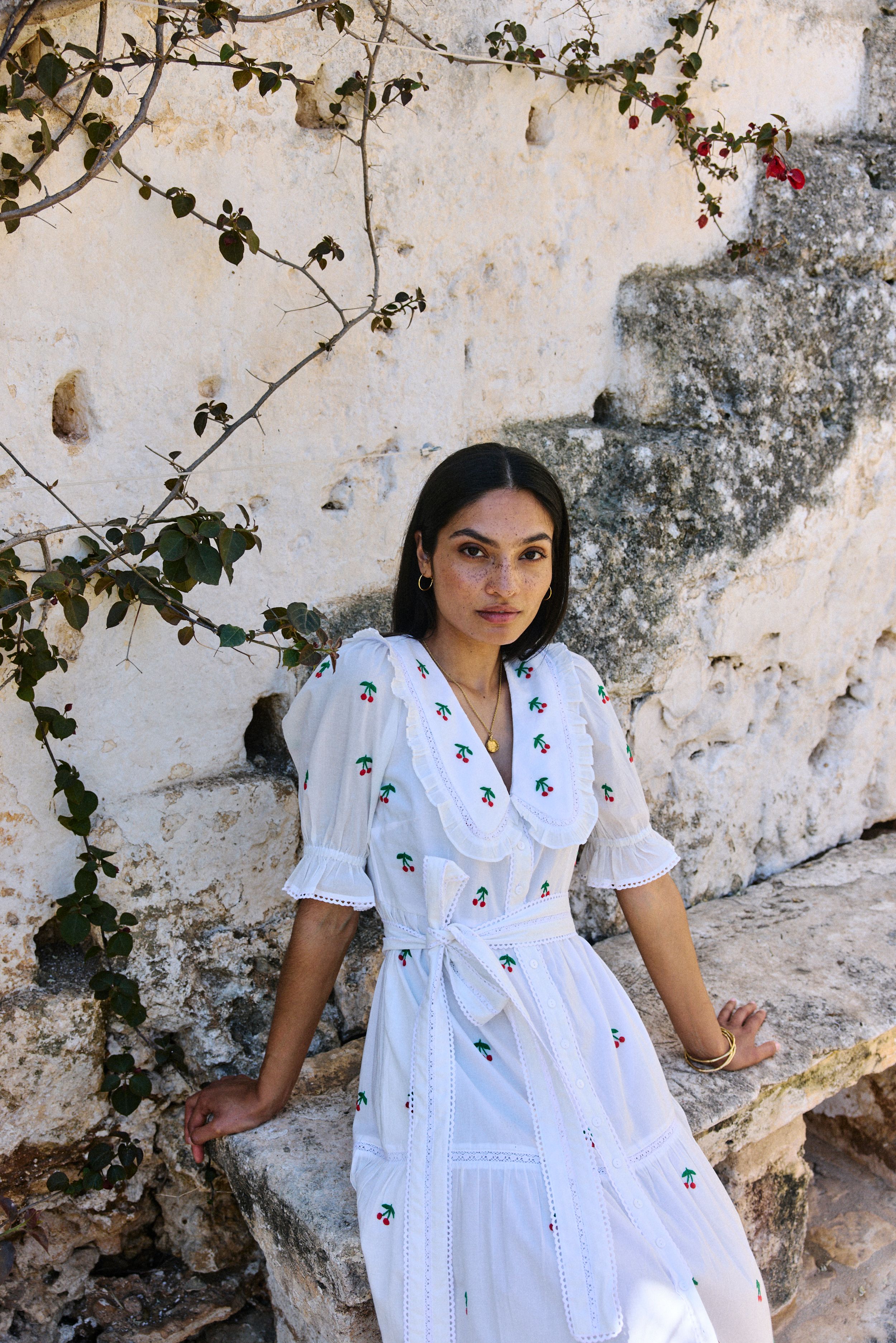 Woman in white embroidered dress stood in front of stone wall