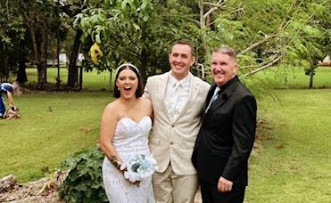 A joyful newly married couple standing with Mark outdoors