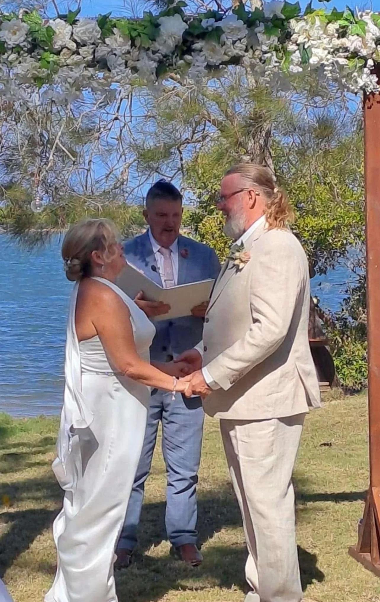 Mark officiating as a couple hold hands beside the water