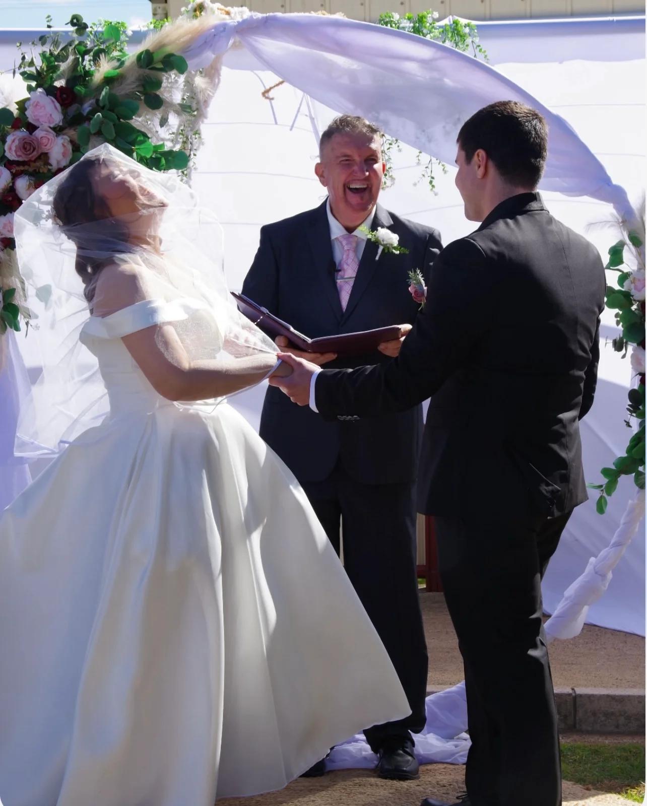 Mark laughing with a couple during a breezy outdoor ceremony