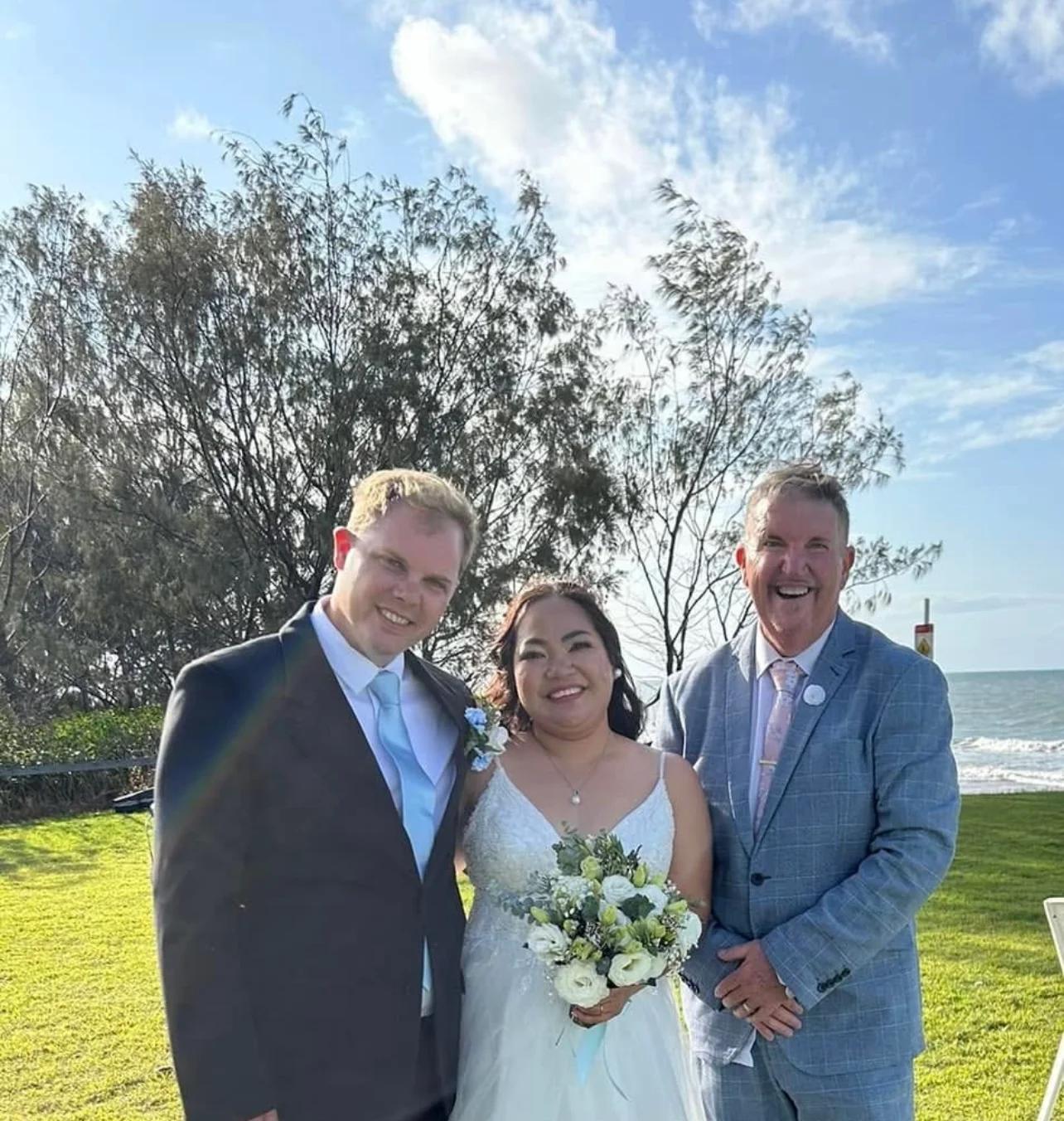 A newly married couple smiling with Mark beside the water