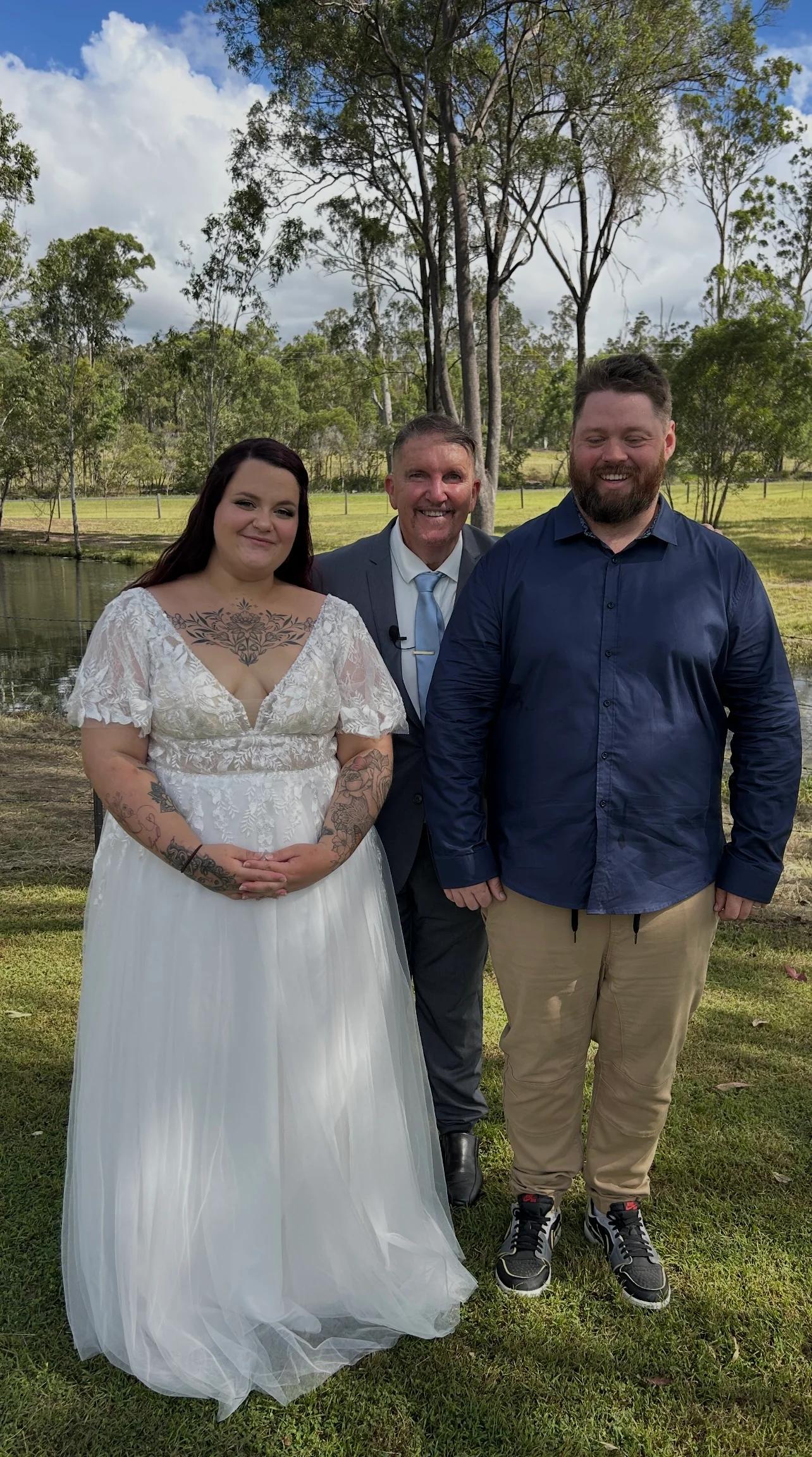 Mark standing with a relaxed couple after their outdoor ceremony