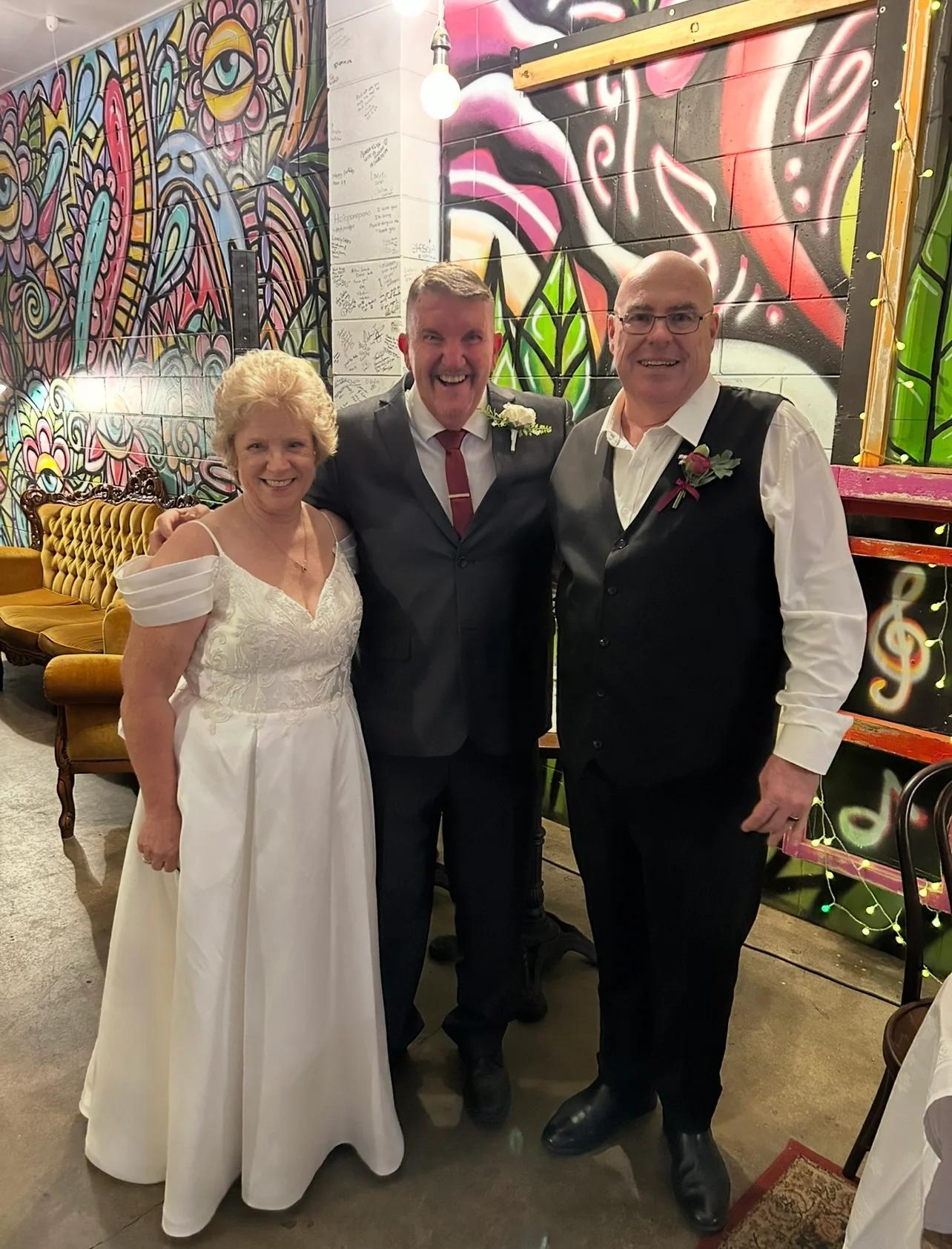 Mark smiling with a newly married couple after their indoor ceremony