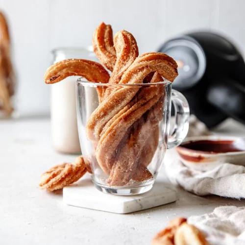 Warm homemade churros with cinnamon topping in a clear mug