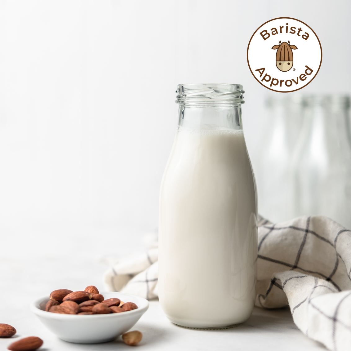 Fresh homemade Pro Almond Milk, presented in a glass jug along with a small bowl of almonds