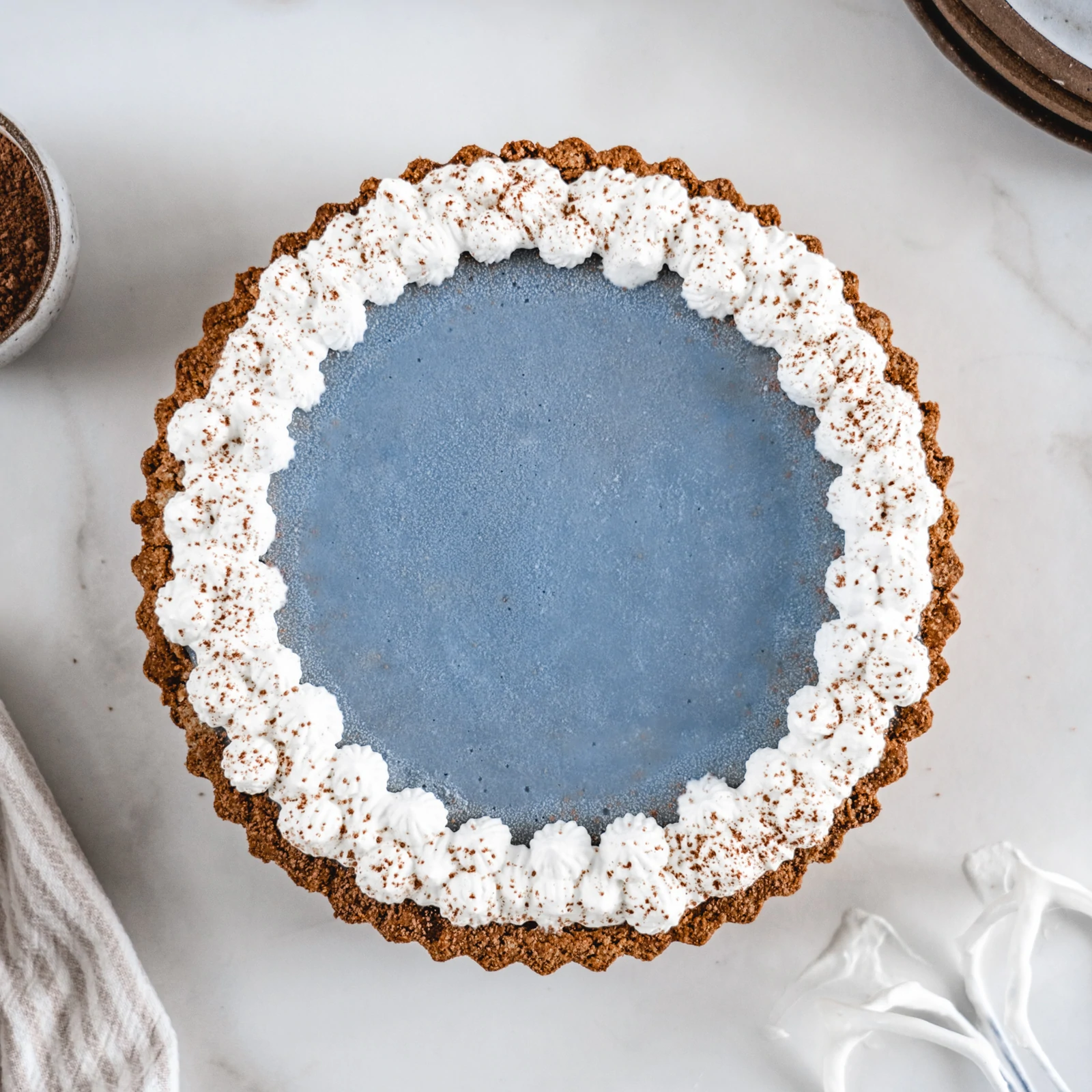 Golden brown crust Almond Cow Tart filled with a blueberry filling and topped with coconut whipped cream