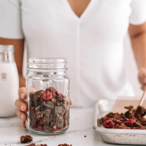vegan double chocolate raspberry granola in a jar with a glass of plant-based milk
