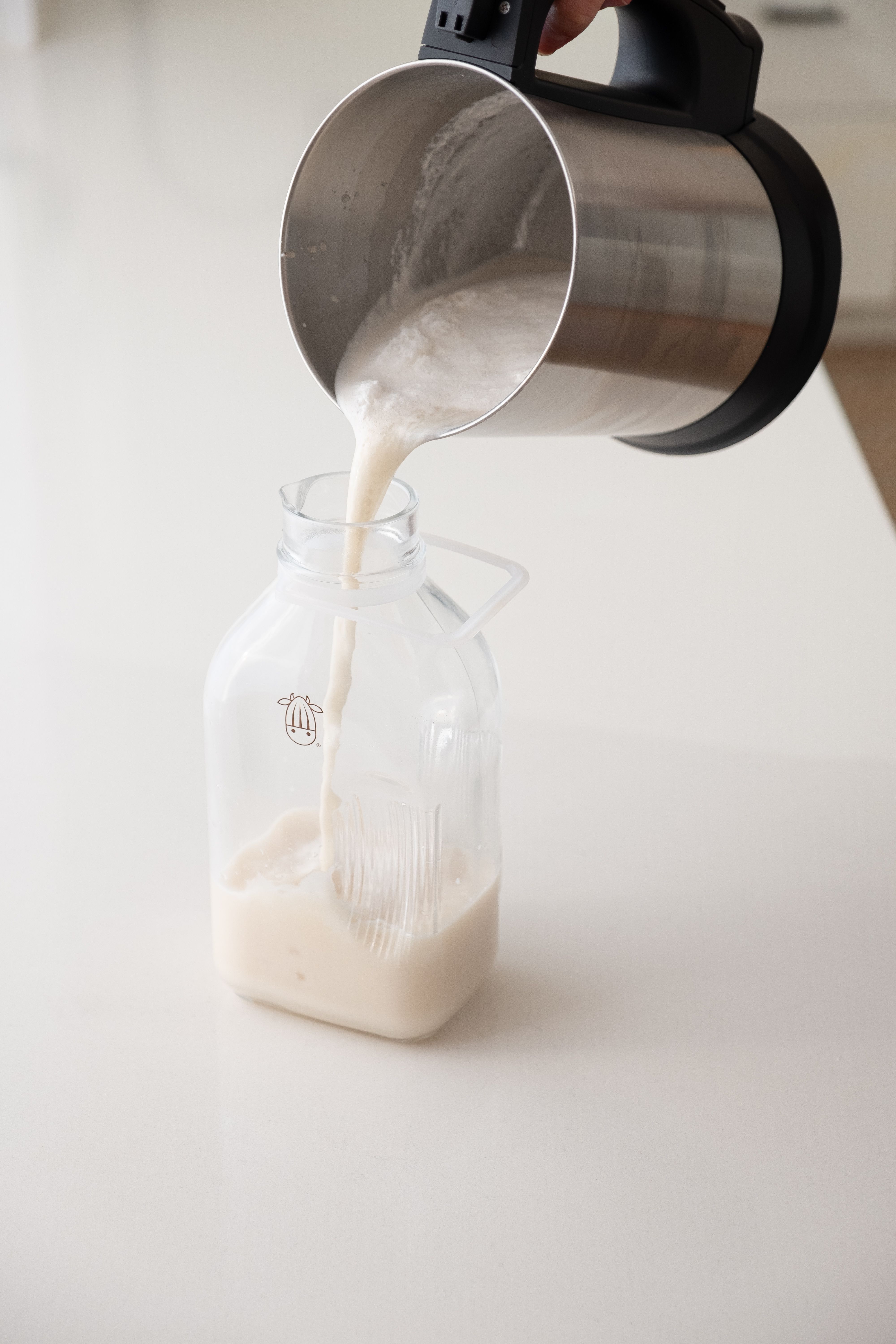 Pouring creamy milk out of the Almond Cow and into a glass jug