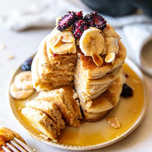 Pancakes stacked on a plate topped with blackberries and bananas