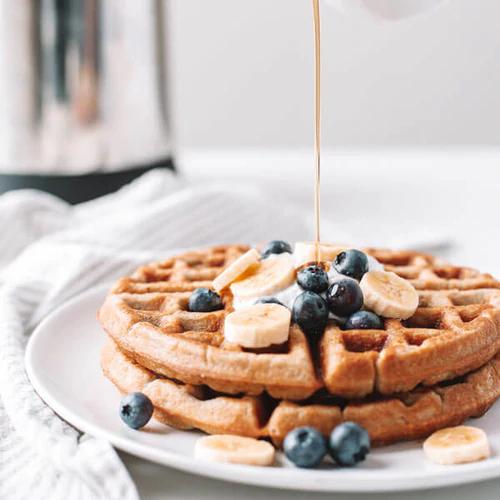 Waffles stacked on a plate with fresh blueberries, bananas, and syrup