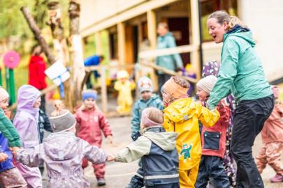 Flere barnehagebarn går i ring sammen med en ansatt i barnehagen mens de synger.