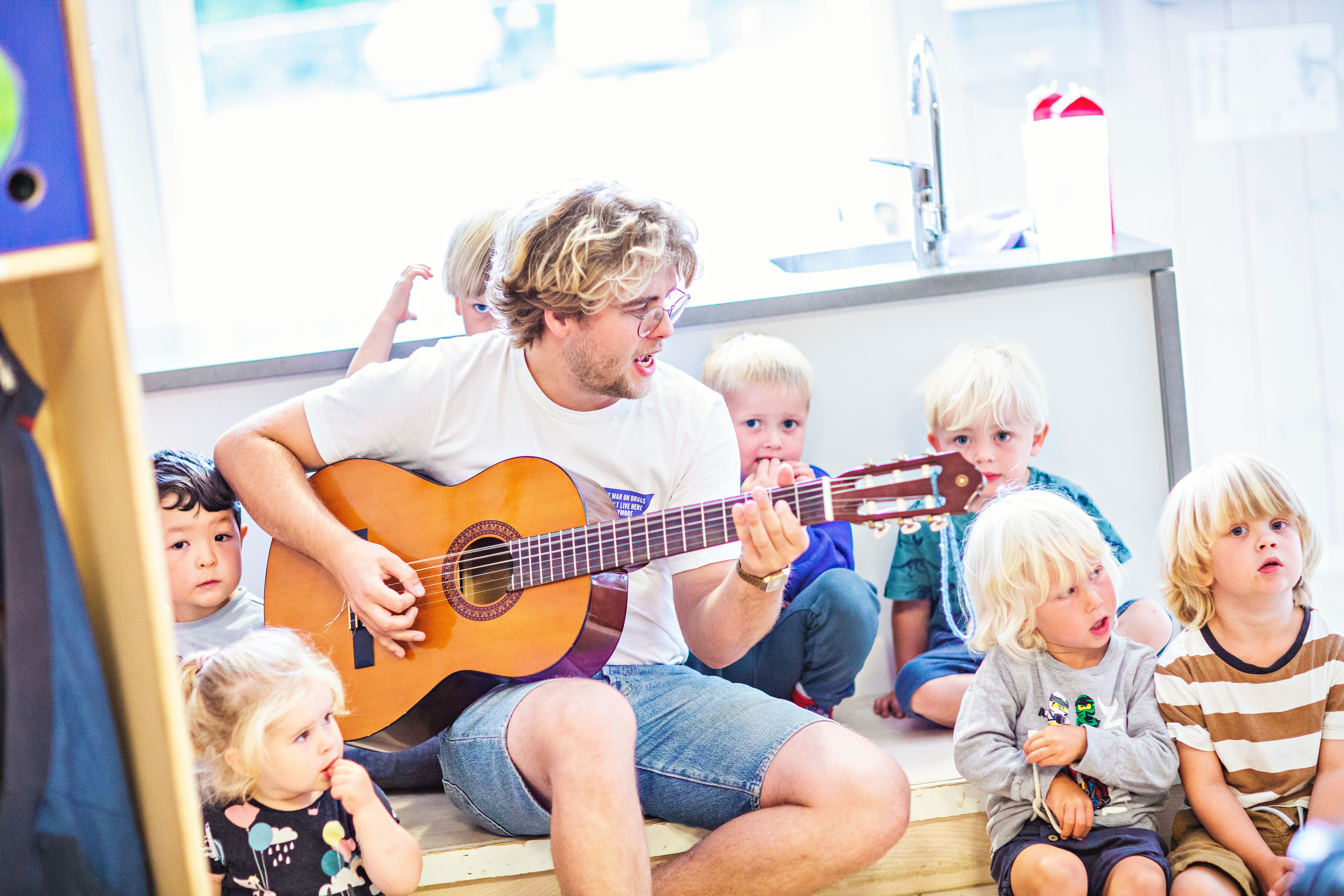 Mann synger og spiller gitar sammen med barn i barnehage