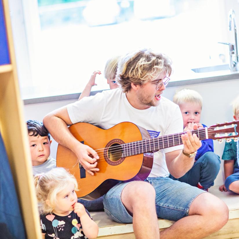 Mann synger og spiller gitar sammen med barn i barnehage