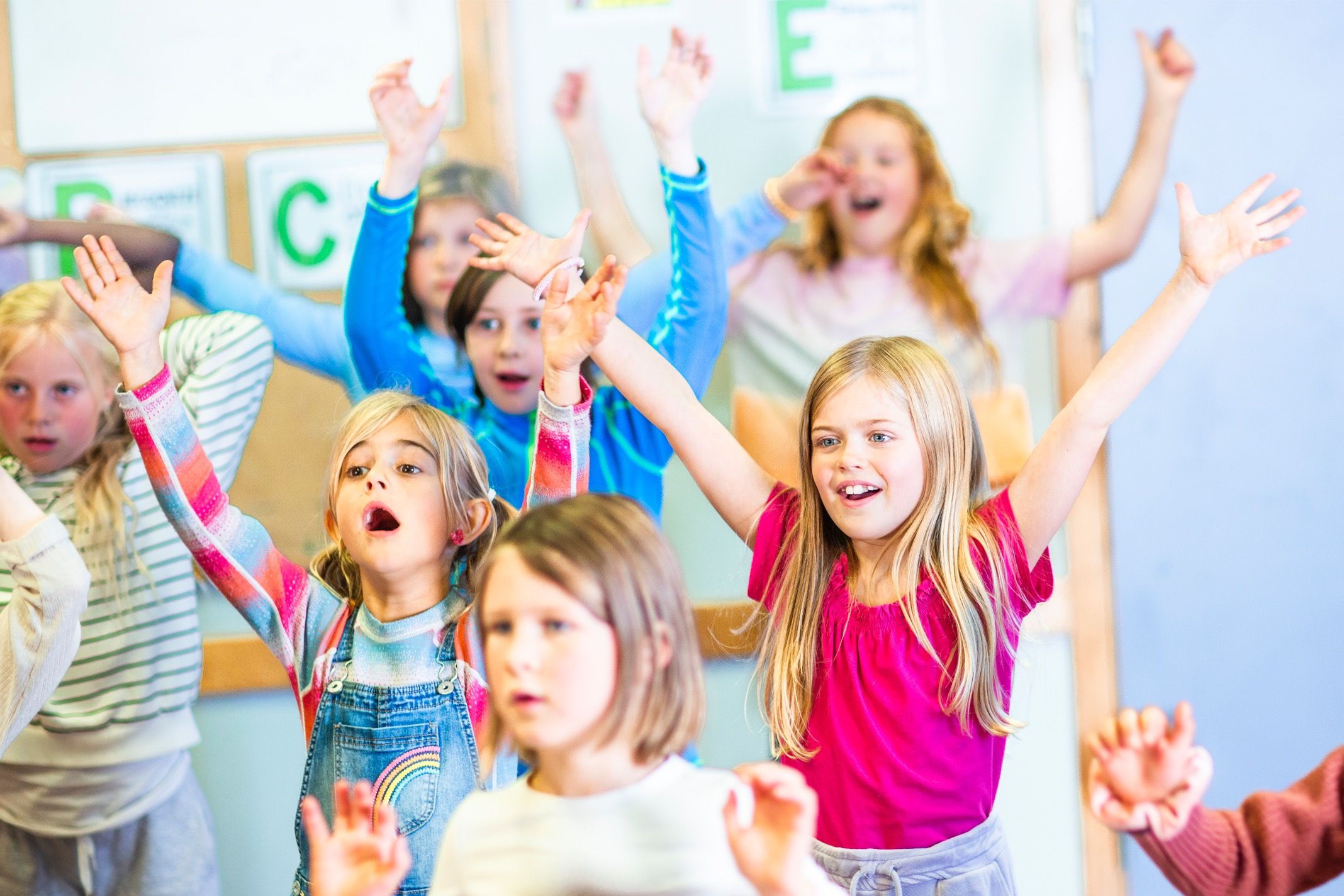 Flere barn på en Syngende skole som synger sammen og rekker hendene i været.