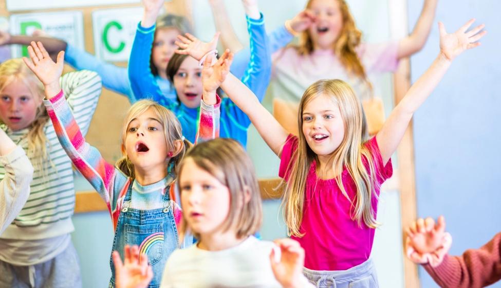 Flere barn på en Syngende skole som synger sammen og rekker hendene i været.