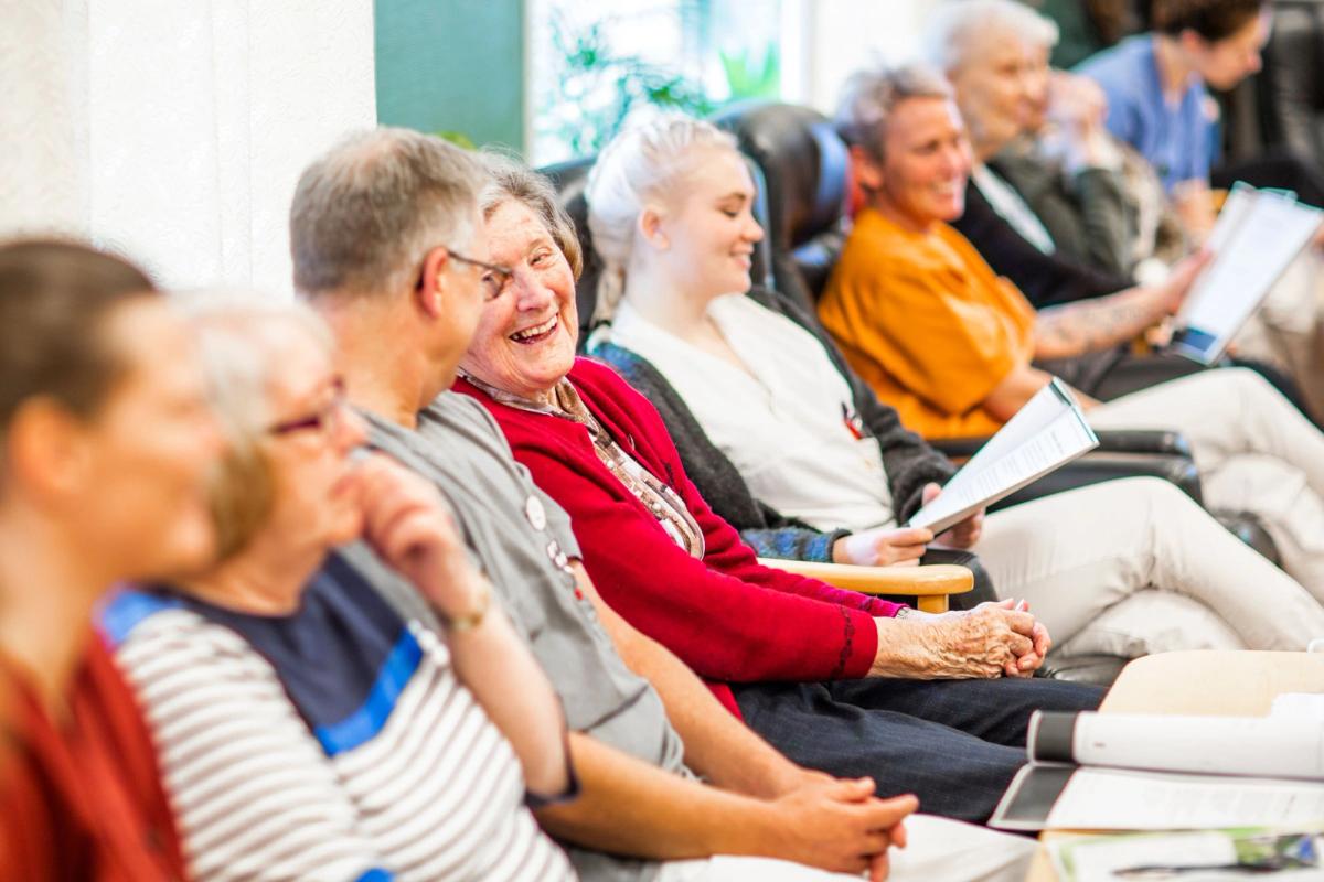 Eldre på institusjon synger sammen med ansatte i dagligstuen.