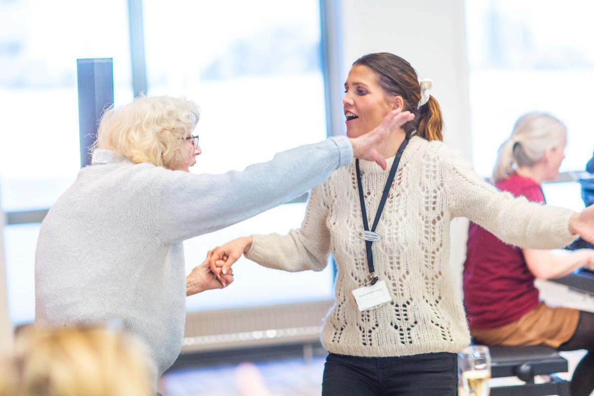 En eldre kvinne synger og danser sammen med en aktivitør på Carpe Diem demenslandsby i Bærum.