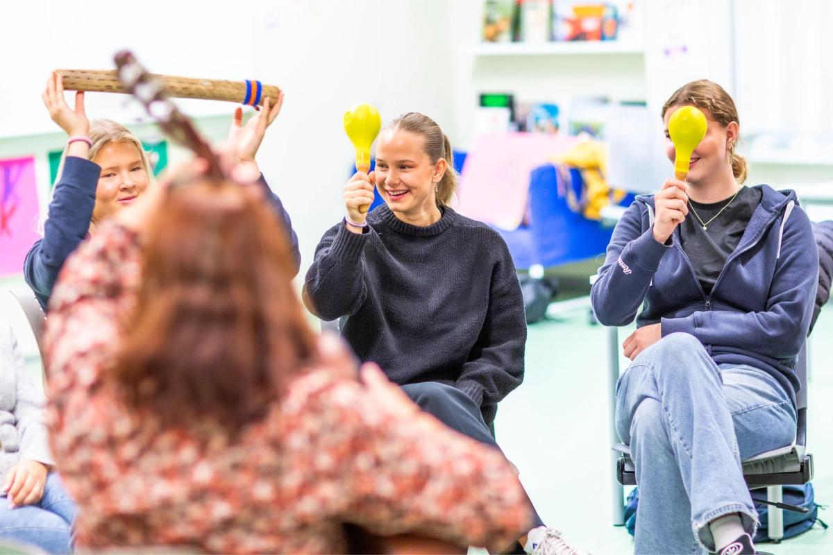 Elever synger og spiller på rytmeinstrumenter i klasserommet