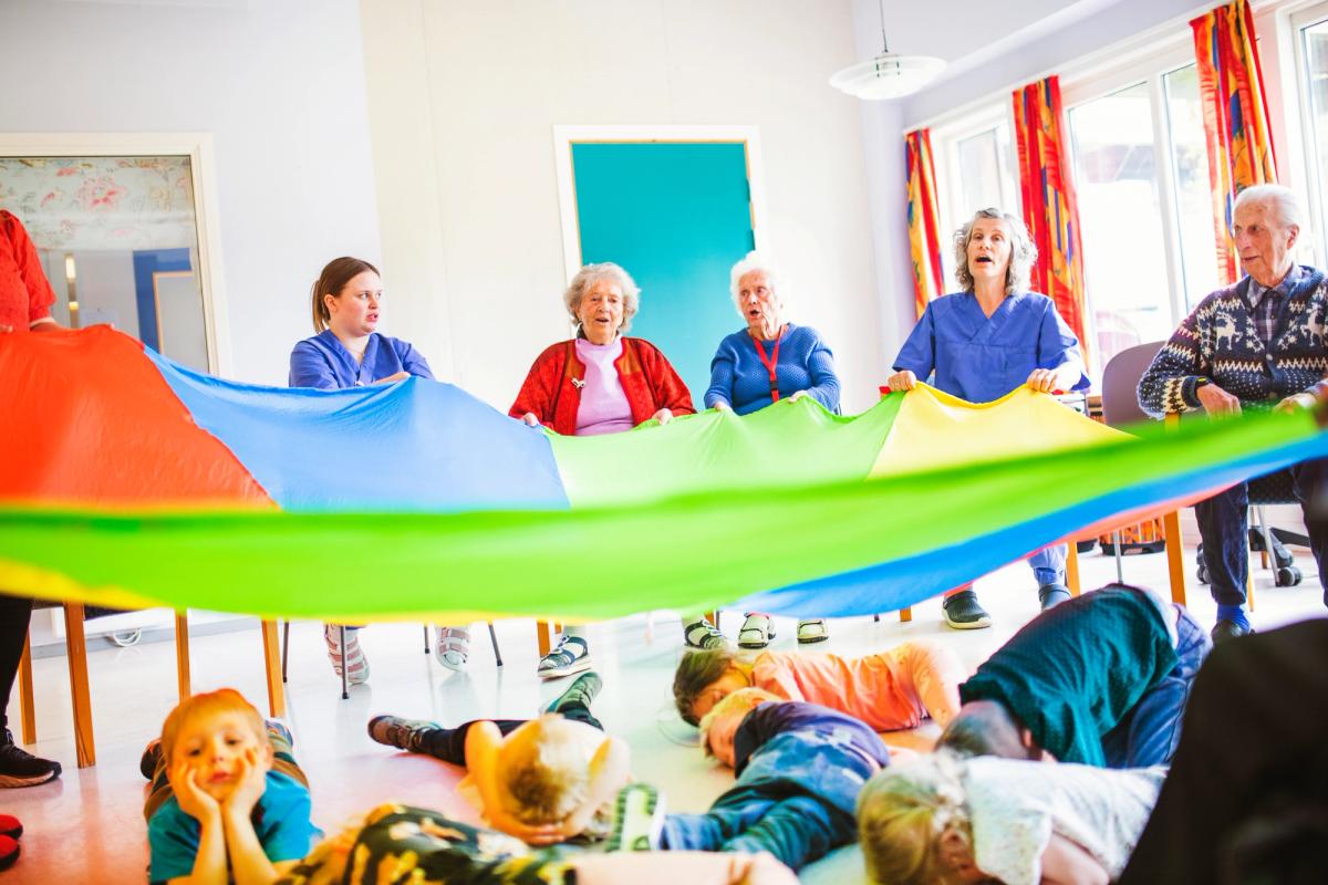 Eldre holder en stor fargefallskjerm over barn som slapper av.