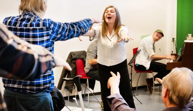Helsekorsang. Kordirigent og eldre mennesker synger og danser sammen.