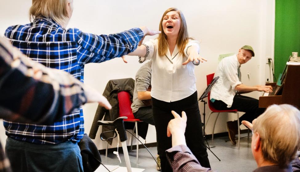 Helsekorsang. Kordirigent og eldre mennesker synger og danser sammen.