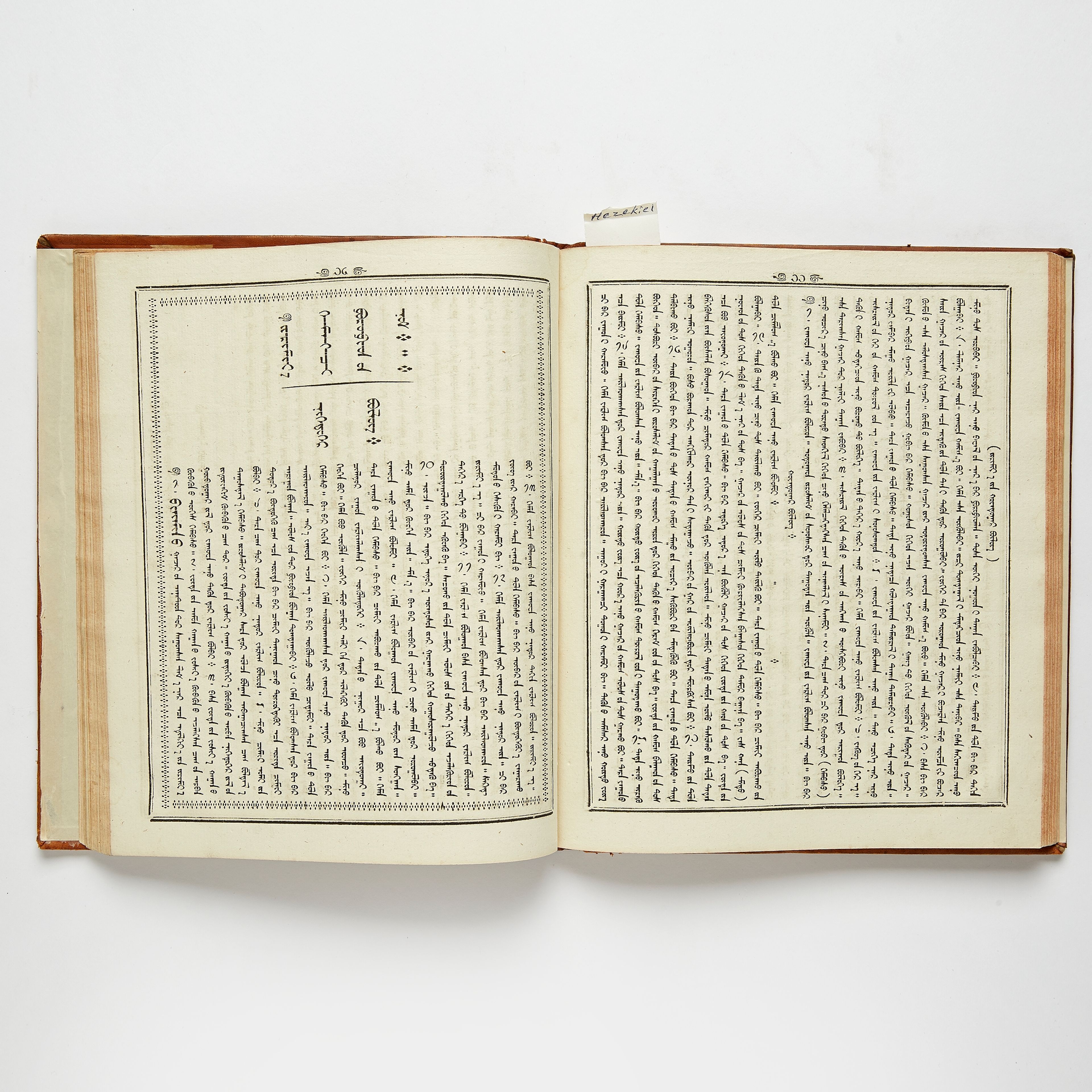 An open book lying flat, both pages printed in the traditional Mongolian script: lines of letters running in vertical columns from top to bottom inside ruled borders, with a small paper tab sticking out at the top.