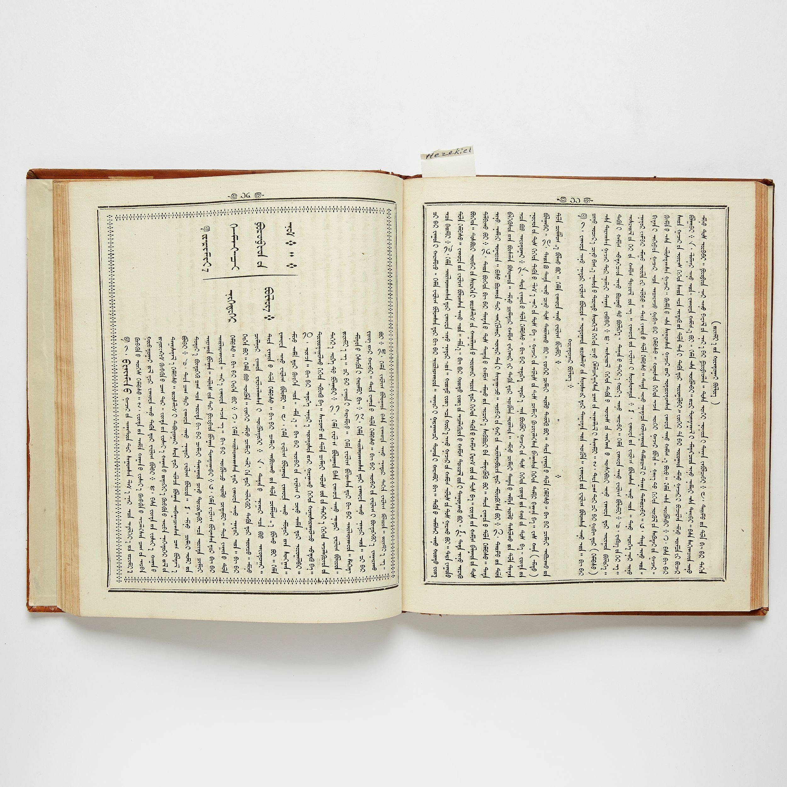 An open book lying flat, both pages printed in the traditional Mongolian script: lines of letters running in vertical columns from top to bottom inside ruled borders, with a small paper tab sticking out at the top.