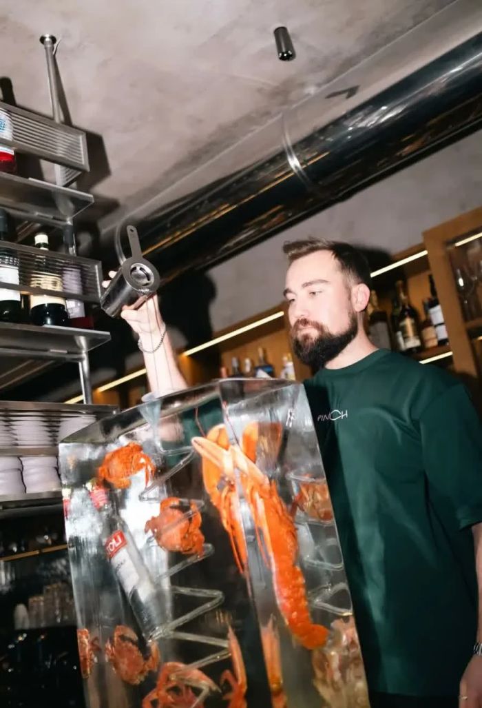Pinch bartender pouring a cocktail beside an ice block with lobsters and crabs inside