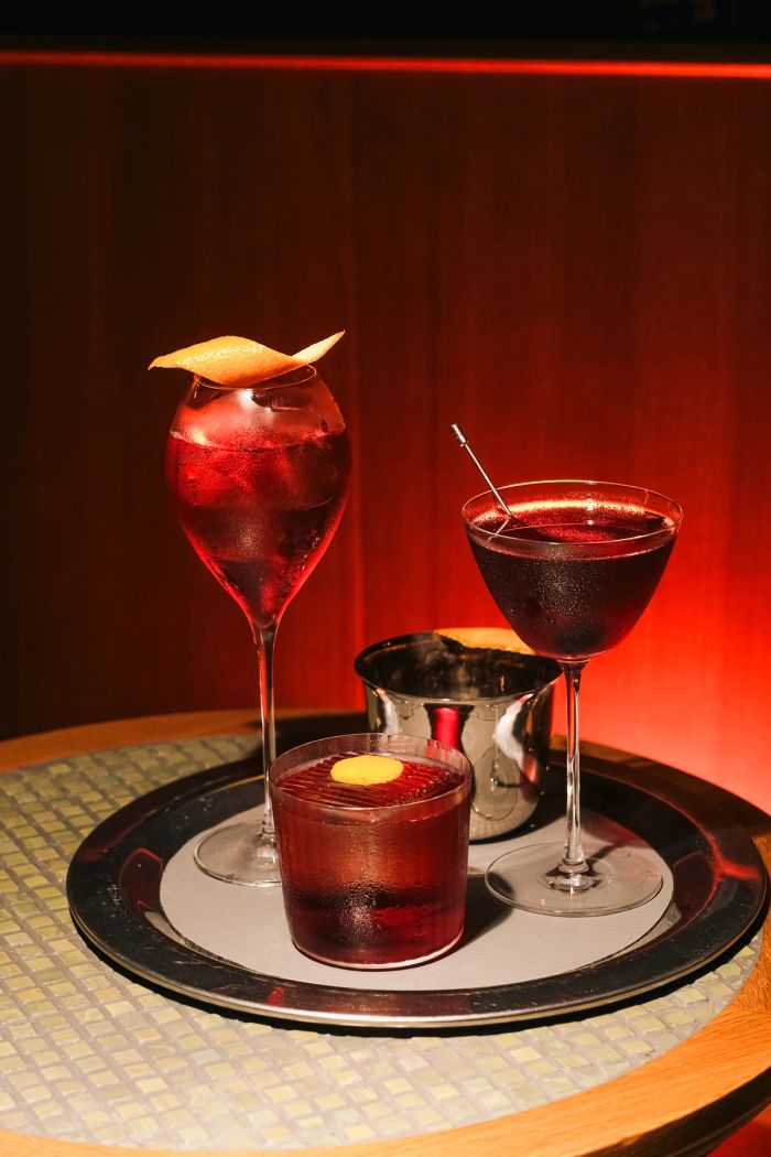 Three red cocktails with citrus garnish on a tray under red light at Pinch Lisbon