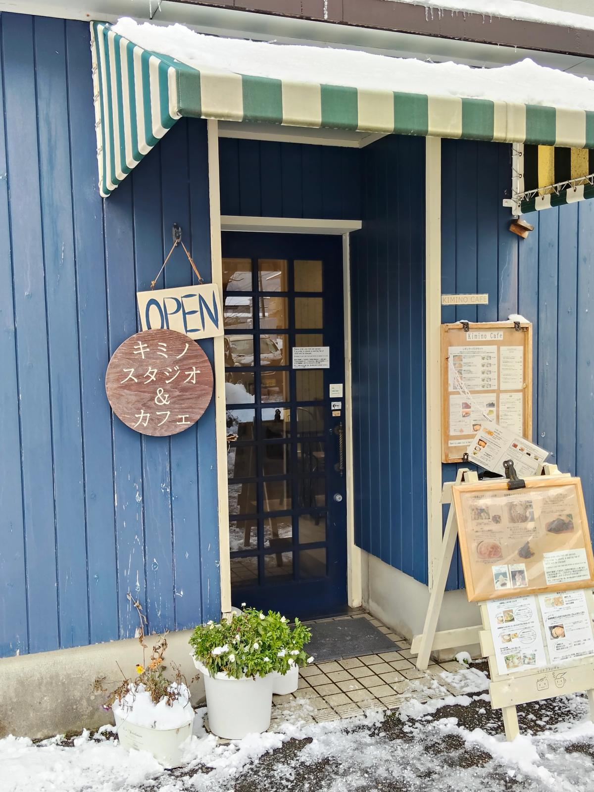 雪をかぶった青い板壁のカフェの入口