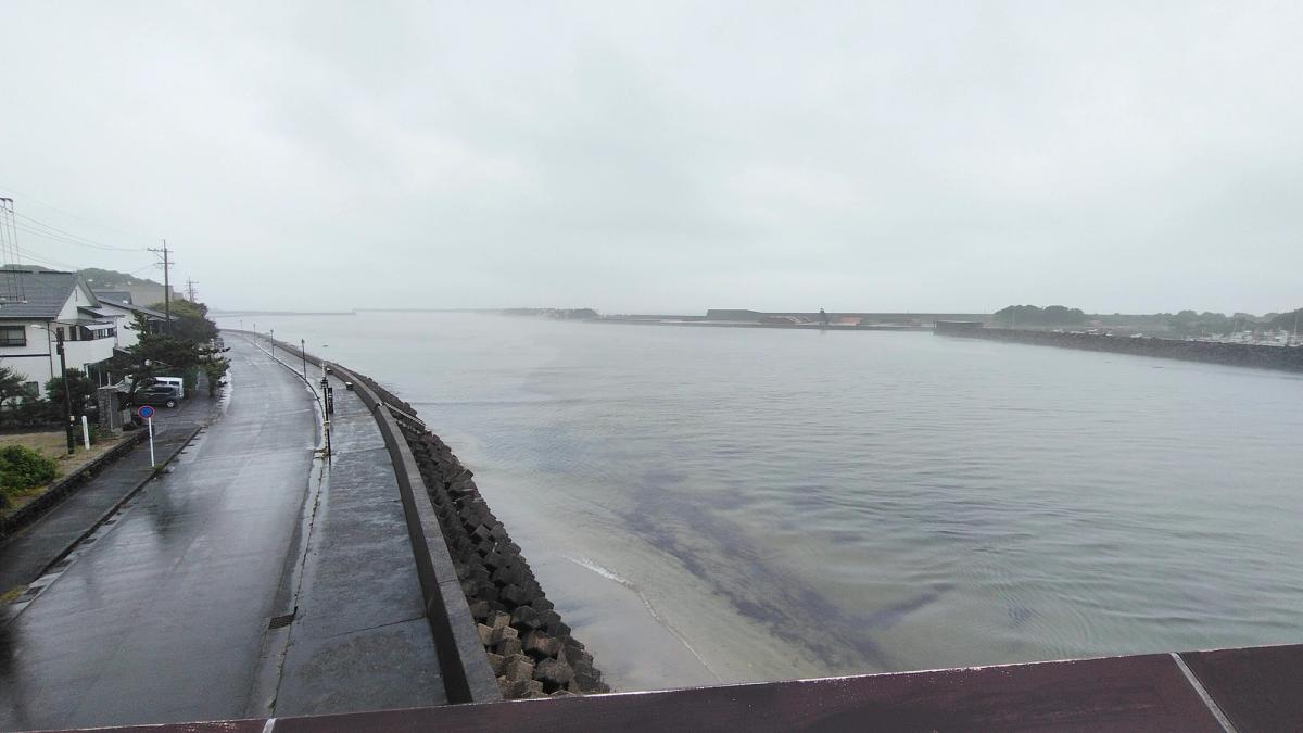 雨に煙る安房川の河口と、海沿いに続く道