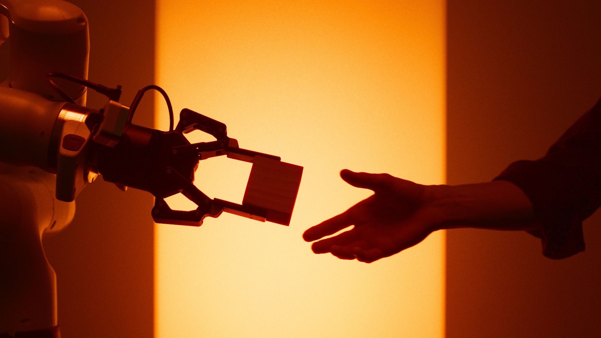 A robot gripper holding a block, reaching towards a human hand.