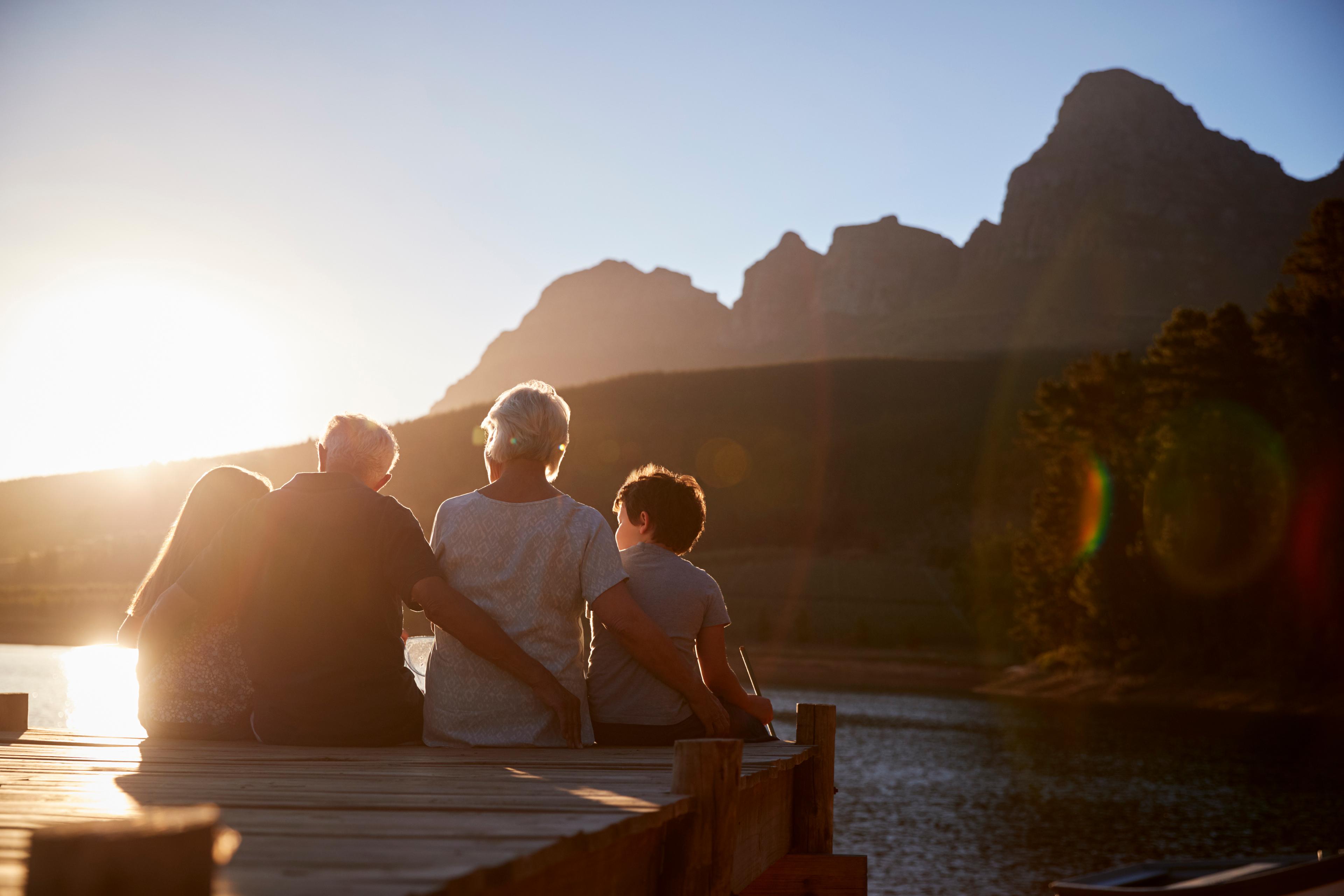 Two adults and two children sitting on a jetty at sunset