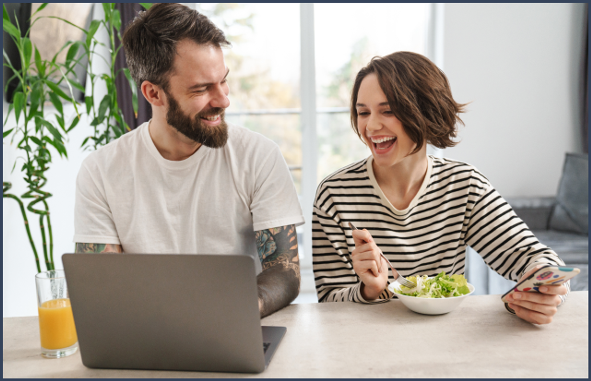 Two people smiling while sitting at a table with a laptop