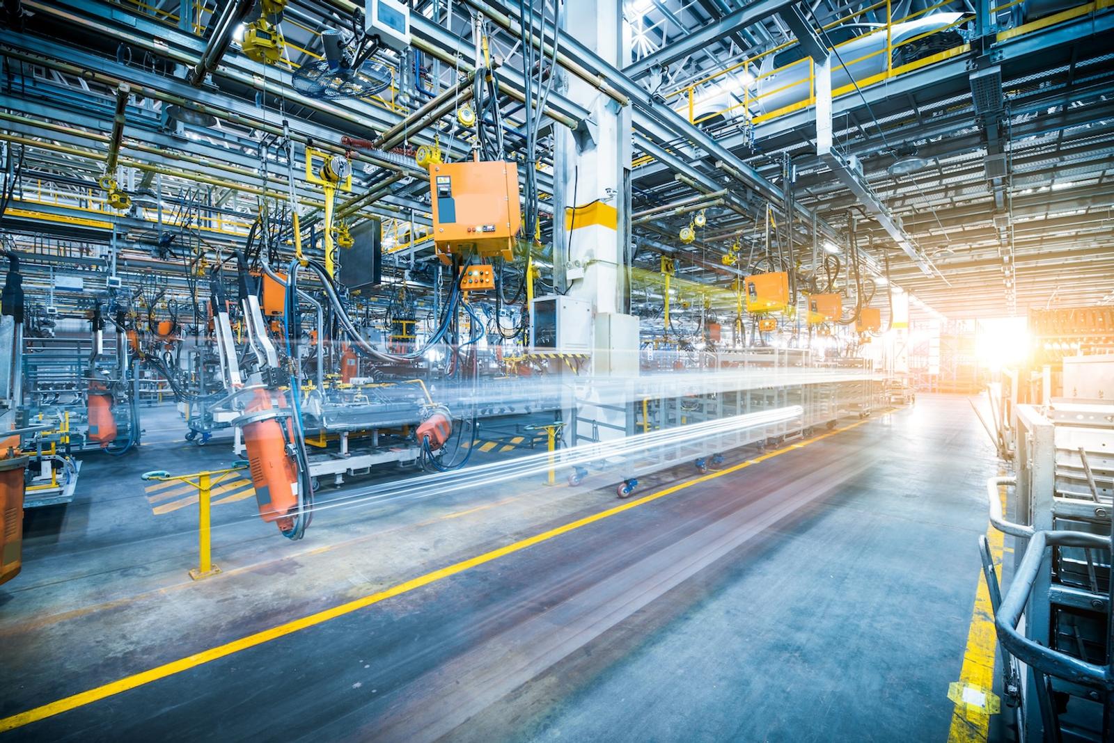Innenraum einer Fabrikhalle mit orangefarbenen Robotern, Foerderanlagen und gelben Bodenmarkierungen