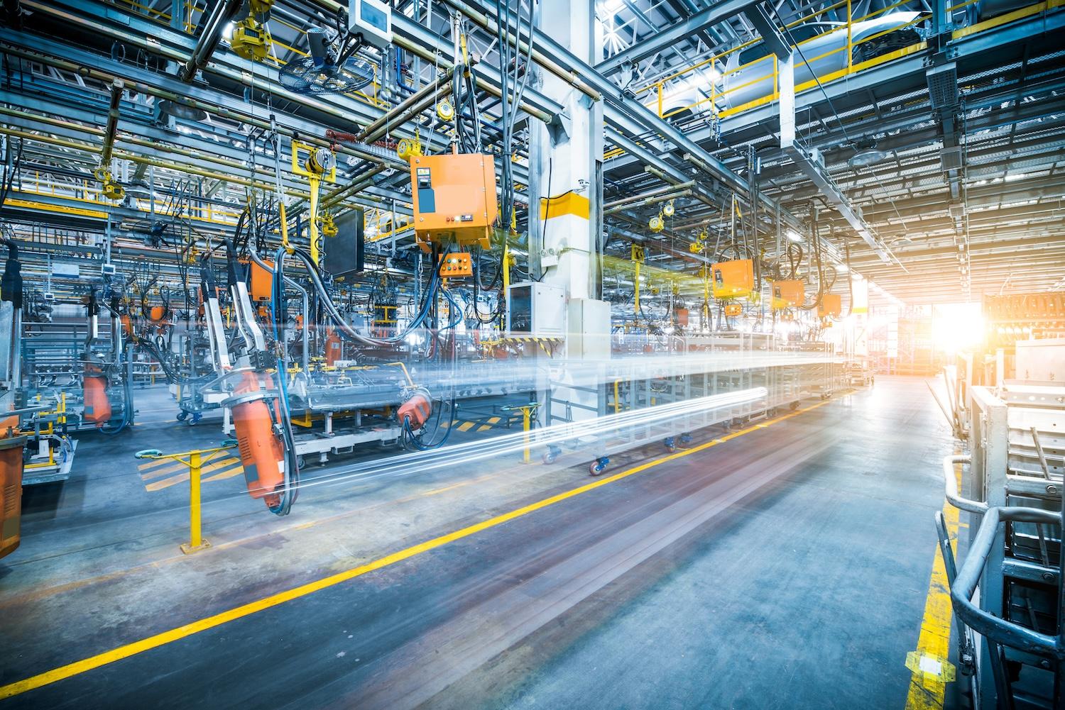 Innenraum einer Fabrikhalle mit orangefarbenen Robotern, Foerderanlagen und gelben Bodenmarkierungen